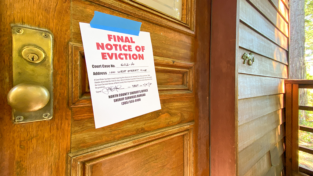 A notice of eviction paper is taped to a wooden door on a house